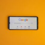 Smartphone displaying Google search page on a vibrant yellow background.