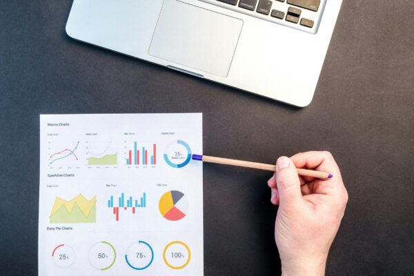 55 consejos SEO que hasta a tu madre le encantarían Hand holding pencil reviewing colorful data charts on desk with laptop.